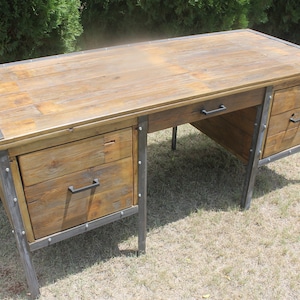 May include: A rustic wooden desk with metal accents and two drawers on each side. The desk has a distressed wood finish and black metal legs.
