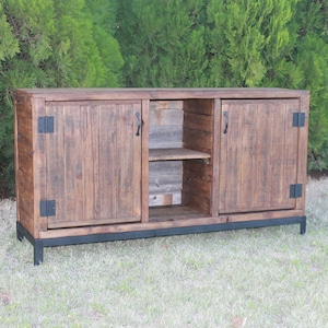 May include: A rustic wooden cabinet with two doors and a shelf. The cabinet has black metal hinges and handles and sits on a black metal base.