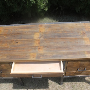 May include: A rustic wooden desk with metal accents and three drawers. The desk has a distressed wood finish and metal hardware. The top drawer is open.