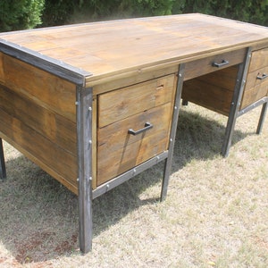 May include: A rustic wooden desk with metal accents and two drawers. The desk has a natural wood finish and black metal legs and drawer pulls.