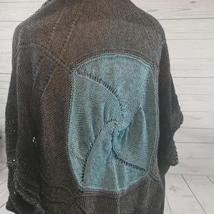 Könnte beinhalten: Ein gestricktes Tuch mit einem Teal- und Graustufen-Farbverlauf. Das Tuch hat ein kreisförmiges Design in der Mitte und ein Spitzenmuster an den Rändern.