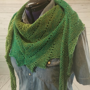 Könnte beinhalten: Ein grünes und hellgrünes gestricktes Tuch mit einem Spitzenmuster. Das Tuch ist über ein Jeanshemd gelegt.