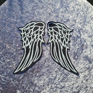 May include: Two black and white angel wings with a detailed design. The wings are on a textured grey surface.