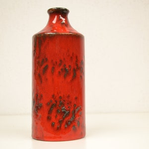 Può includere: Un vaso in ceramica rosso con una smaltatura testurizzata e screziata. Il vaso ha una forma cilindrica con un collo stretto.