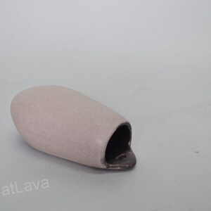 May include: A light pink ceramic wall vase with a dark brown opening. The vase is shaped like a rounded, elongated oval.