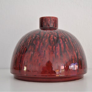 Puede incluir: Un jarrón de cerámica rojo en forma de cúpula con detalles de esmalte negro. El jarrón tiene un acabado liso y brillante.