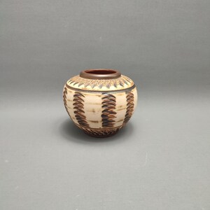 May include: A small, round ceramic vase with a brown and white geometric pattern. The vase has a slightly flared opening and a rounded bottom.
