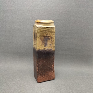 May include: A small, rectangular ceramic vase with a brown and yellow glaze. The vase has a slightly uneven, rustic finish.