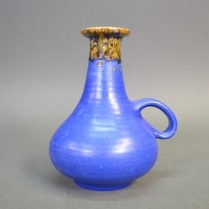 May include: A blue ceramic vase with a brown and gold glaze on the top. The vase has a rounded body and a handle.