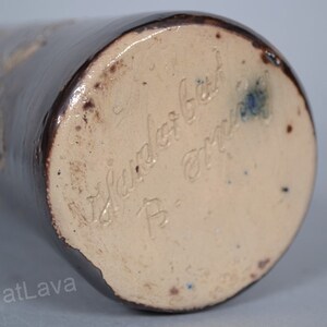 May include: Close-up of the base of a brown ceramic vase with a light brown glaze. The vase is signed "W. Sander Geb. B. - Germany".