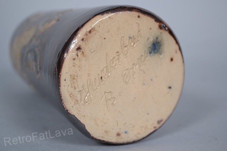 May include: Close-up of the base of a brown ceramic vase with a light brown glaze. The vase is signed "W. Sander Geb. B. - Germany".