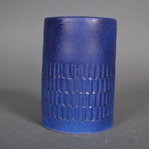 May include: A tall, cylindrical blue ceramic vase with a textured pattern. The vase has a smooth, glossy finish.