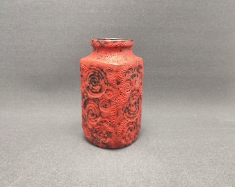 Puede incluir: Un pequeño jarrón de cerámica rojo con una superficie texturizada y un patrón floral negro. El jarrón mide aproximadamente 10 cm de alto.