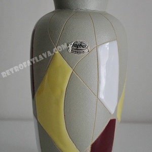 May include: A grey ceramic vase with a geometric design in yellow, white and burgundy. The vase has a label that reads "Jasba Keramik".