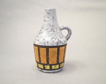 May include: A white ceramic vase with a brown and gold geometric pattern. The vase has a rounded body and a small handle.