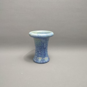 Puede incluir: Un pequeño jarrón de cerámica azul y verde con la parte superior acampanada y un cuerpo texturizado y acanalado.