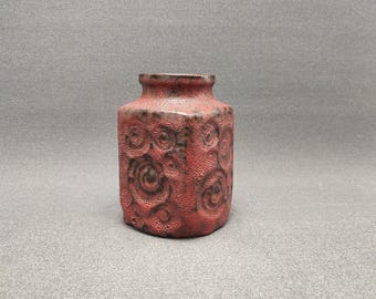 May include: A small, red, square-shaped ceramic vase with a textured surface and a floral design.