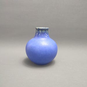 May include: A small, round, blue ceramic vase with white speckles. The vase has a narrow neck and a wide base.
