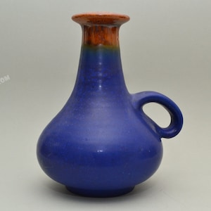 May include: A blue ceramic vase with a brown rim and a handle. The vase has a rounded body and a narrow neck.