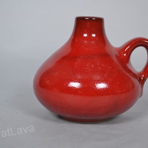 May include: A red ceramic vase with a rounded body and a single handle. The vase has a glossy finish.