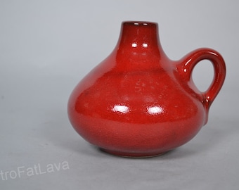 Puede incluir: Un jarrón de cerámica rojo con cuerpo redondeado y una sola asa. El jarrón tiene un acabado brillante.
