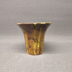 Könnte beinhalten: Eine kleine, braune Keramikvase mit grünem Glase, das an den Seiten herunterläuft. Die Vase hat einen ausgestellten oberen Rand und einen abgerundeten Boden.