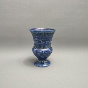 May include: A small blue ceramic vase with a geometric pattern. The vase has a wide mouth and a narrow base.