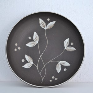 May include: A brown ceramic plate with a white floral design. The plate has a simple, elegant design with stylised flowers and dots.