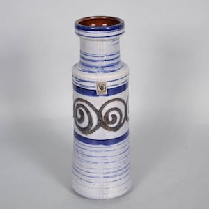 Puede incluir: Un jarrón de cerámica blanca con rayas y remolinos azules y marrones. El jarrón tiene un borde marrón y una banda azul alrededor del medio.