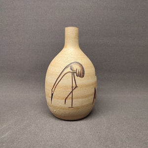 May include: A small, tan ceramic vase with a brown bird design. The vase has a narrow neck and a rounded body.
