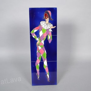 May include: A set of three blue ceramic tiles featuring a colourful illustration of a jester wearing a mask and a hat. The jester is wearing a pink, green and white diamond patterned costume.