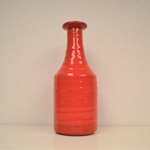 May include: A tall, red ceramic vase with a narrow neck and a rounded base. The vase has a glossy finish and a striped pattern.