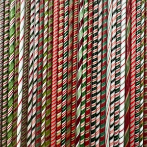 May include: A collection of long, thin candy canes arranged vertically in a tight row. Each candy cane features a distinct spiral pattern of red, green, and white stripes, creating a repetitive, colorful texture across the entire frame.