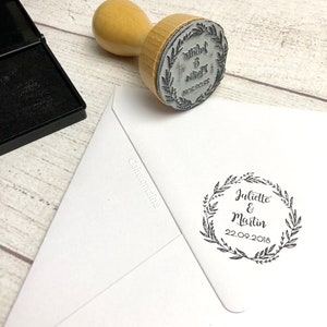 Peut inclure: Une enveloppe blanche avec un tampon d'encre noire qui indique "Juliette & Martin 22.09.2018" à l'intérieur d'une couronne de feuilles.
