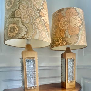 Puede incluir: Dos lámparas de mesa vintage con pantallas estampadas con motivos florales en beige, marrón y verde oliva. Las bases de madera tienen un diseño rectangular con un panel de vidrio texturizado. Las lámparas están sobre una mesa redonda de madera.
