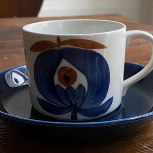 May include: A white ceramic coffee cup with a blue and brown floral design, sitting on a blue saucer.