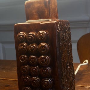 May include: A brown ceramic table lamp with a white shade and a textured design of concentric circles. The lamp has a white cord.