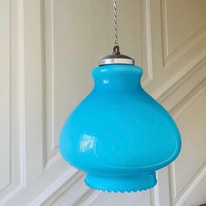 Puede incluir: Lámpara colgante vintage de cristal azul turquesa. La lámpara tiene una pantalla redondeada en forma de campana con borde festoneado y una tapa de metal plateado. Cuelga de una cadena plateada.