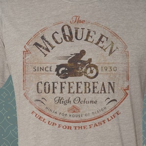 May include: A heather grey t-shirt with a vintage-style logo featuring a motorcycle rider and the text "The McQueen Coffeebean High Octane Ninja for House of Design Fuel Up for the Fast Life".