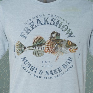 May include: Light blue t-shirt with a graphic of a fish and the text "Bermuda Triangle Freakshow Sushi & Sake Bar Est. 2000 Creepy Raw Fish Delicacies"