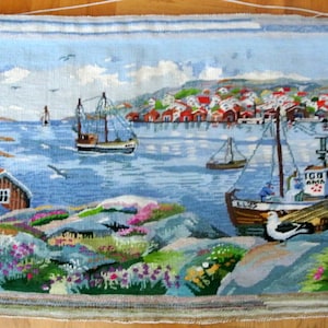 May include: A colorful needlepoint wall hanging depicting a seascape with sailboats, a small town, and a seagull. The scene is set against a blue sky with white clouds.