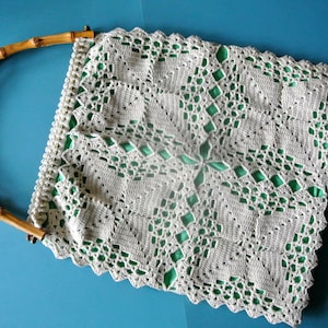 May include: A white crocheted bag with a green lining and a natural bamboo handle.