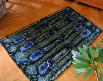 May include: A rectangular shag rug featuring a deep color palette of black, forest green, and various shades of blue. The design consists of repeating vertical bands and textured, tufted circular and oval motifs arranged in a structured pattern.