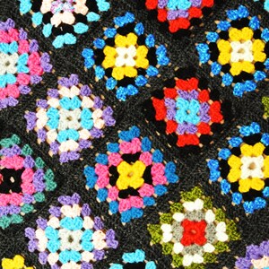 Puede incluir: Una manta de ganchillo colorida con fondo negro y cuadrados de diferentes colores, incluyendo rojo, azul, amarillo, verde y morado.