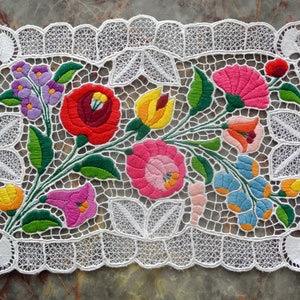 Puede incluir: Mantel de encaje blanco con diseño floral bordado en rojo, rosa, amarillo, azul y verde.