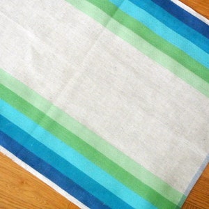 May include: A white linen kitchen towel with blue, green, and light blue stripes. The towel is folded in half and has a white border.