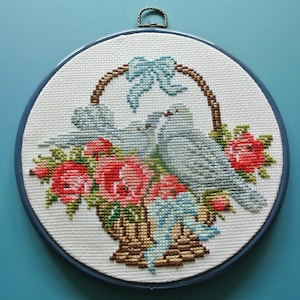 1980 年代のヴィンテージ、大きめの丸いクロスステッチ刺繍、多色の花とバスケットの中の鳩のモチーフの壁掛け、白い綿、青いプラスチックフレーム