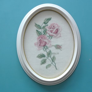 Vintage sueco de la década de 1970 hecho a mano punto de cruz rosa / verde rosa flor motivo lino bordado pared colgante con marco de plástico blanco hueso ovalado