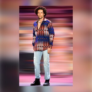 May include: A man wearing a blue, red, and white patterned long-sleeve shirt with a light blue denim shirt and black boots.