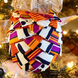 May include: A handmade Christmas ornament shaped like a pine cone, made from colorful fabric with a gold ribbon at the top. The ornament features a variety of patterns and colors, including orange, purple, black, and white. The ornament is a unique and festive addition to any Christmas tree.
